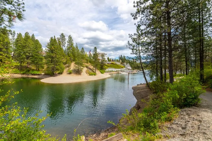 The small bay and sandy beach at Black Bay Park on the Spokane River in Post Falls, lined with pine trees.